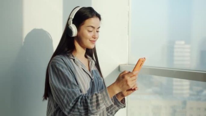漂亮的亚洲女孩在家里用智能手机和耳机听音乐