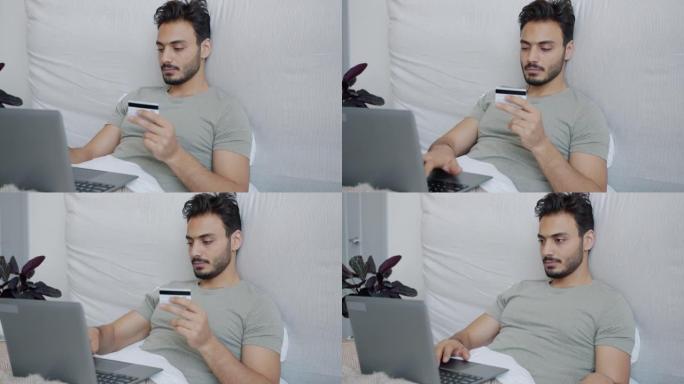 中东人使用笔记本电脑和信用卡在线购物，在床上享受幸福