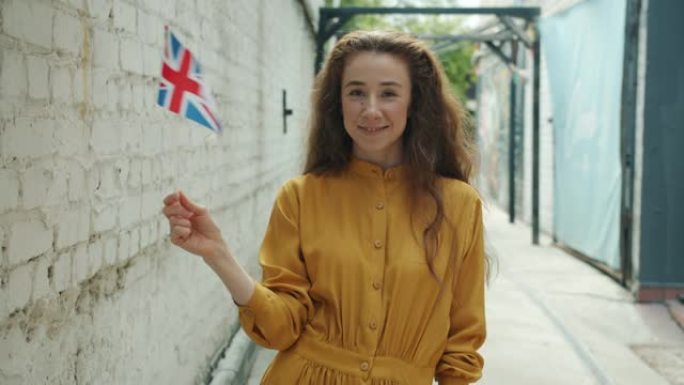 迷人的年轻女性游客的肖像，举着英国国旗站在城市街道上微笑
