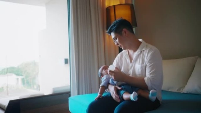 亚洲单身父亲从沙发上的婴儿奶瓶给婴儿喂奶。与新生儿成为父亲的时刻。