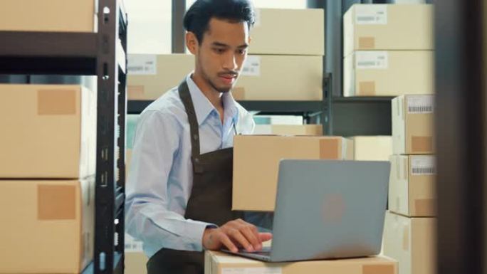 亚洲商业伙伴男人穿正式衬衫拿着纸板箱使用笔记本电脑检查库存在线库存数据程序在仓库交货客户。创业小企业