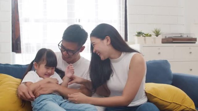 快乐快乐的亚洲家庭爸爸、妈妈和女儿在家里过生日时拥抱在沙发上玩耍。