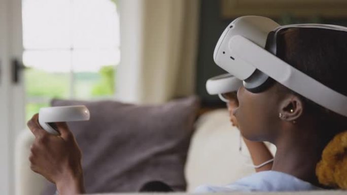 女人在家躺在沙发上戴着带控制器的VR耳机，并与AR技术互动