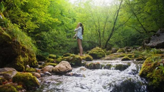SLO MO年轻女子在森林中的溪流中享受新鲜的空气与和平