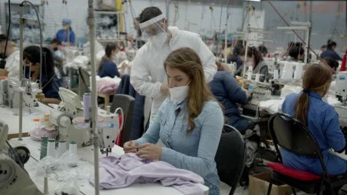 穿着生物安全服，遮阳板和口罩的男主管要求生产线上的女员工正确佩戴口罩