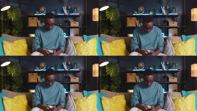 移动游戏快乐的年轻z世代黑人男学生沉迷于在家中沙发上使用智能手机在线玩游戏。