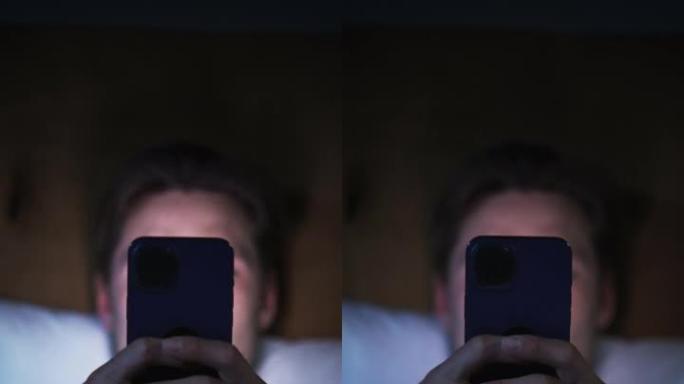 垂直屏幕: 白人男子晚上在家床上使用智能手机。帅哥浏览社交媒体，阅读新闻，网上购物，深夜。手持手机