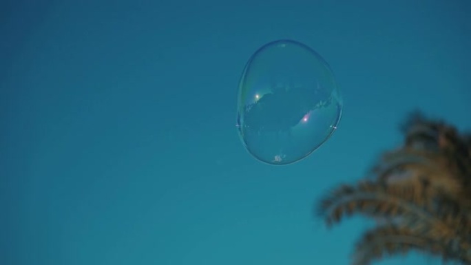 一个肥皂泡在蓝色的天空中飞起来。快乐顽皮的泡沫鼓风机的人在夏日享受户外的生日乐趣。户外游戏，肥皂水浮