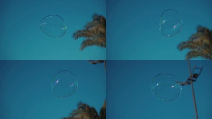 一个肥皂泡在蓝色的天空中飞起来。快乐顽皮的泡沫鼓风机的人在夏日享受户外的生日乐趣。户外游戏，肥皂水浮