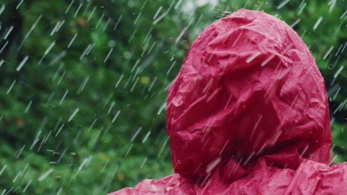 一个穿着红色雨衣的快乐女人的肖像，笑着享受在雨下。女性成年人感激水和自然的祝福，周围是树木。她在享受