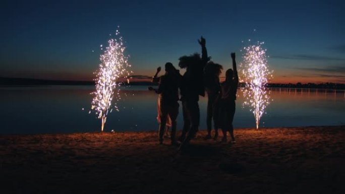 开朗的年轻人晚上在海滩上跳舞的学生用烟花点燃