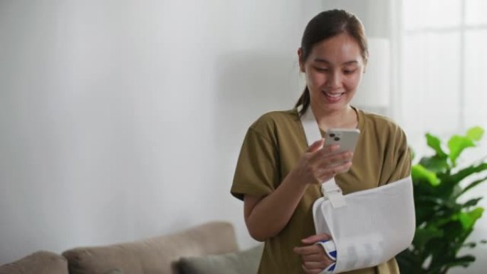 女人自信微笑的事故后断臂，戴上手臂夹板进行治疗并握着智能手机，快乐的亚洲女性吊带支撑手孤立在白色背景