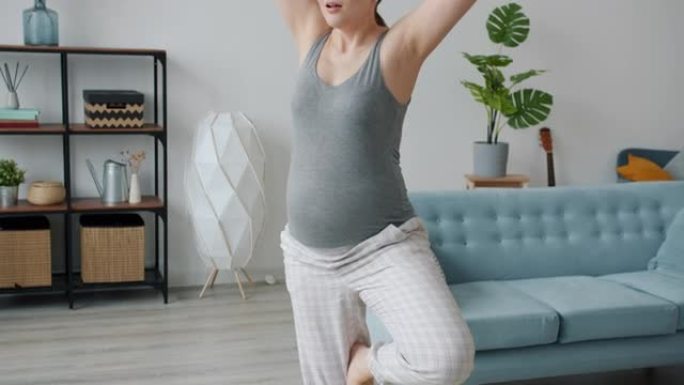 身材健美的孕妇在家里独自进行单腿训练的瑜伽平衡肖像