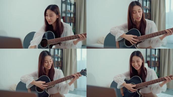 快乐的年轻女子专注于学习用笔记本电脑弹吉他坐在家里的客厅