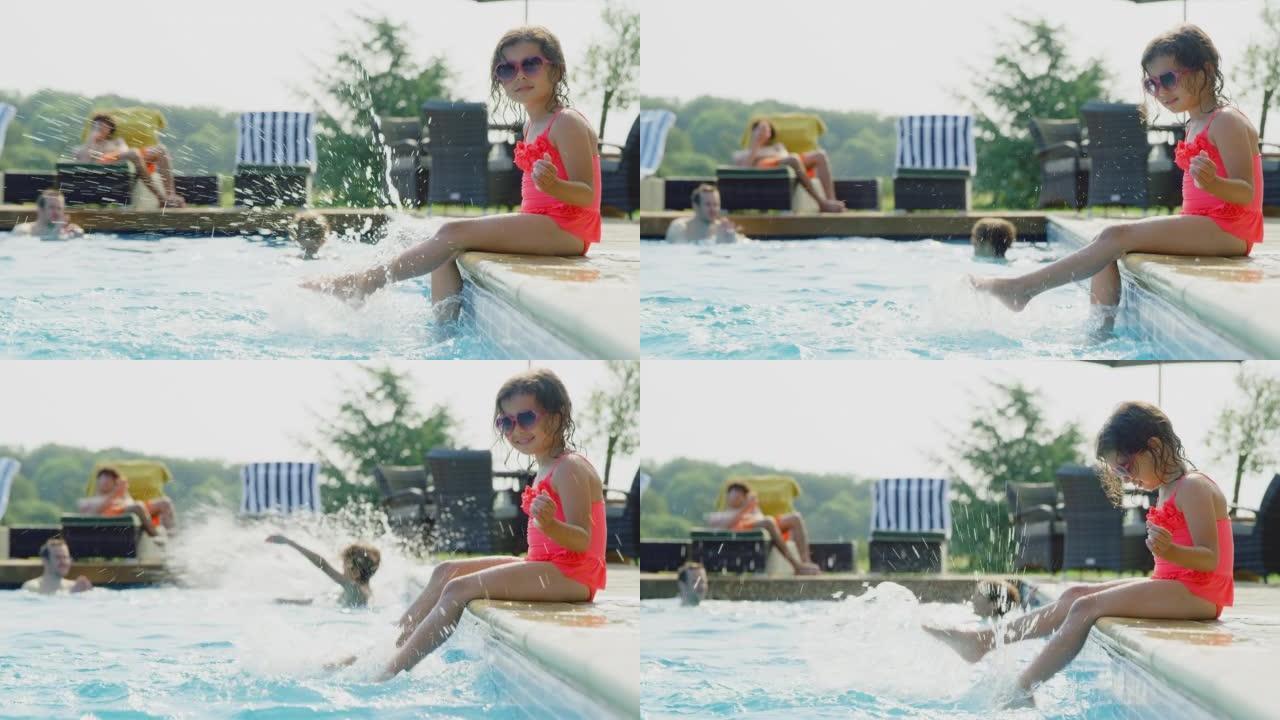 女孩坐在室外游泳池的边缘，在家庭暑假里把脚溅在水里 -- 慢动作拍摄