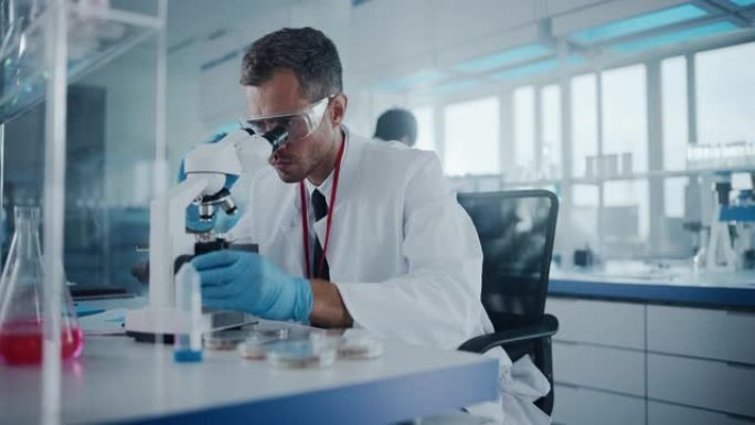 医学发展实验室: 男性科学家在显微镜下观察，分析培养皿样品。背景大制药实验室与专家进行医学，生物技术