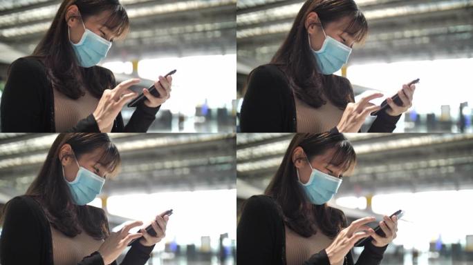 亚洲女子戴口罩保护在机场使用智能手机，新常态概念