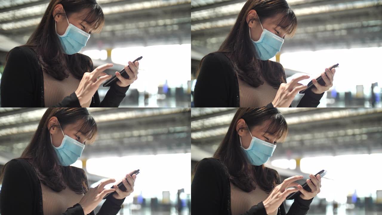 亚洲女子戴口罩保护在机场使用智能手机，新常态概念