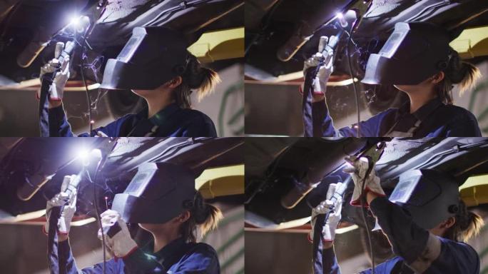 在汽车服务站的汽车下戴焊接头盔的女机械师