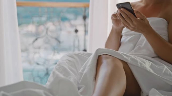 SLO MO Mid成年女性在海景房间的床上使用智能手机