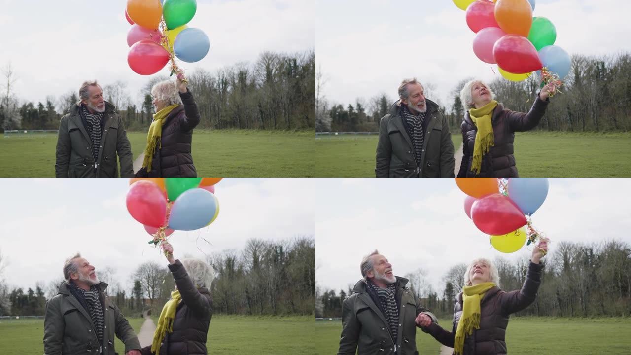 充满爱心的老年夫妇拿着气球享受秋天或冬天一起穿过公园