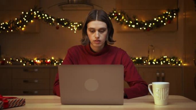 一位穿着红色毛衣的迷人年轻女子坐在厨房的桌子旁，在笔记本电脑上工作