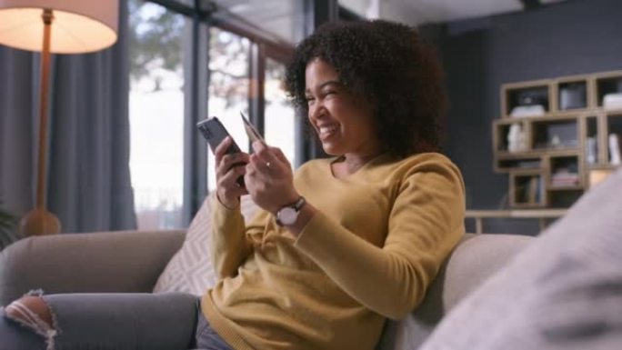 4k视频片段，一名年轻女子使用带有信用卡的智能手机并在家中沙发上欢呼