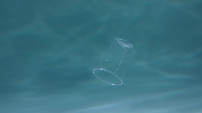 被塑料污染的海洋。浅蓝色背景慢动作的特写废弃一次性杯子漂浮在水下