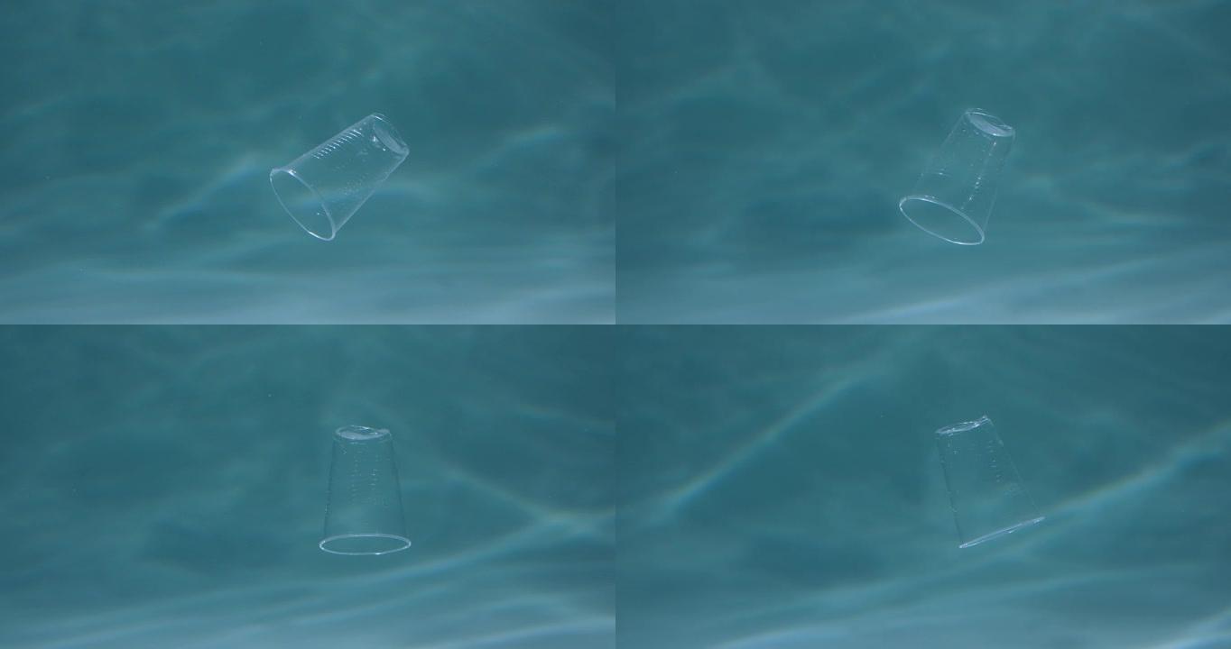 被塑料污染的海洋。浅蓝色背景慢动作的特写废弃一次性杯子漂浮在水下