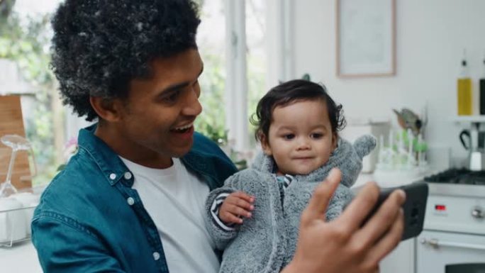 父亲和婴儿使用智能手机视频聊天快乐爸爸抱着蹒跚学步的孩子在社交媒体上与朋友分享父亲的生活方式享受移动