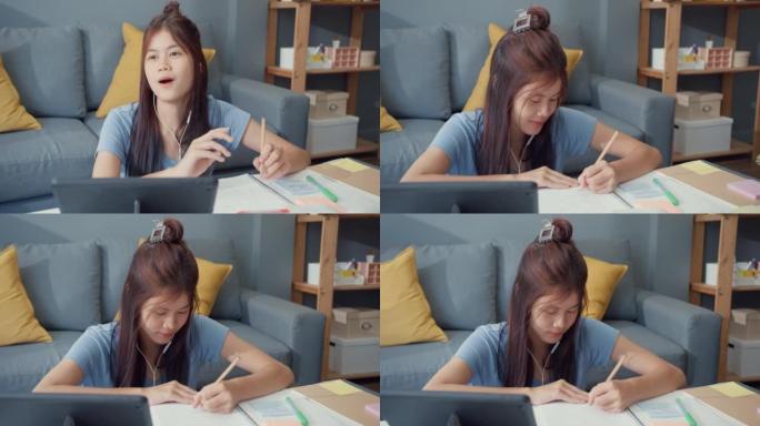年轻的亚洲女孩少年，戴着休闲装耳机，使用数字平板电脑在线学习在家客厅写讲座笔记本。隔离教育在线电子学