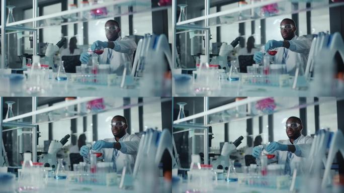 非裔美国男性科学家戴着护目镜，在实验室的试管中混合化学物质。英俊的黑人微生物学家在现代实验室工作，拥
