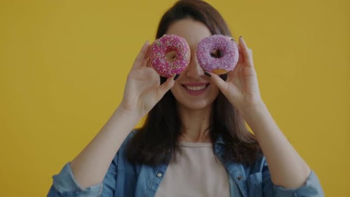 快乐女士的肖像与甜甜圈在黄色背景上微笑着看着相机