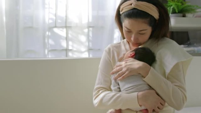 单身母亲坐在家里的婴儿室时，将刚出生的男婴抱在肩上。