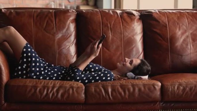 躺在沙发上的女人戴着耳机在智能手机上听音乐