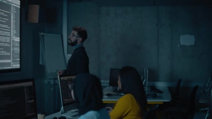 老师在黑暗的大学教室里为不同种族的男女学生提供计算机科学讲座。用编程代码投影幻灯片。解释信息技术。