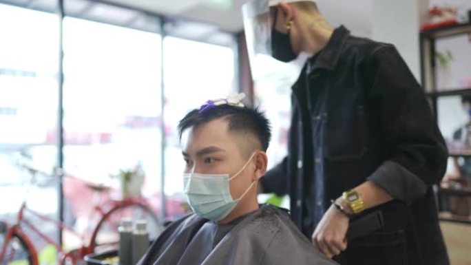 穿着防护服的亚洲华人发型师在发廊为他的顾客理发