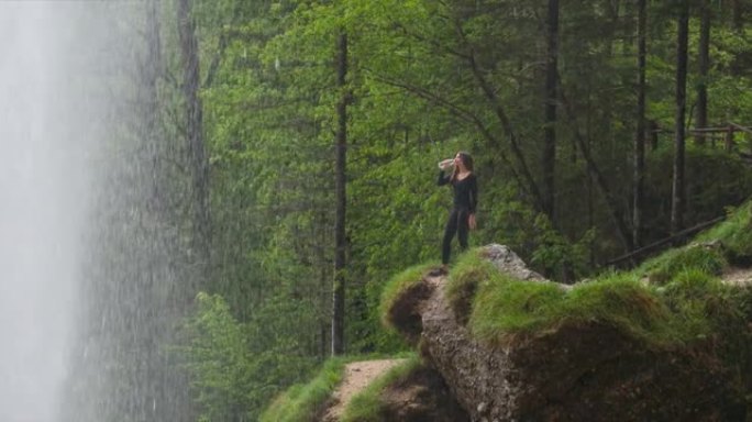 年轻女徒步旅行者在瀑布前喝水