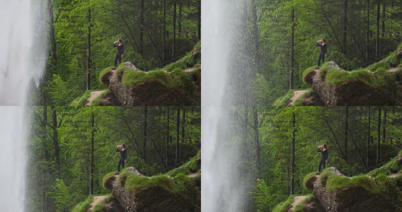 年轻女徒步旅行者在瀑布前喝水