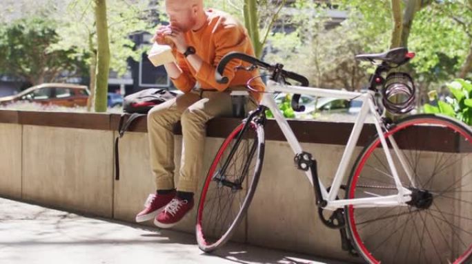 白化病非裔美国男子，长发lock坐在公园里，骑自行车吃三明治