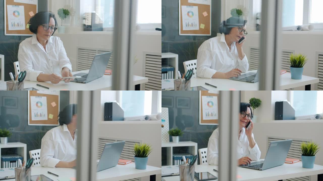 开朗的女人用笔记本电脑打字，然后用手机聊天，独自在办公室工作，微笑着