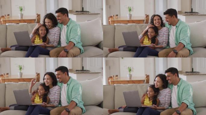 快乐的西班牙裔父母和女儿坐在沙发上使用笔记本电脑