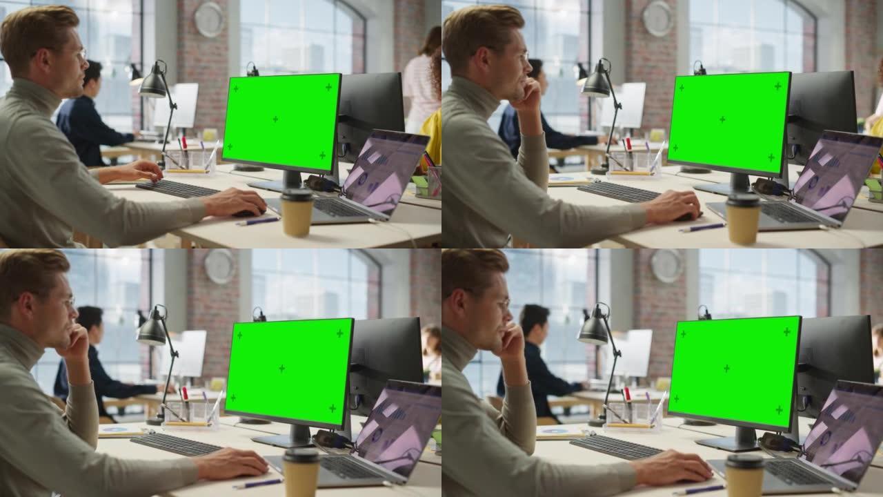 白人创意年轻人的肖像白天在绿色屏幕电脑上工作在现代繁忙的办公室。项目经理在使用台式计算机时微笑。放大