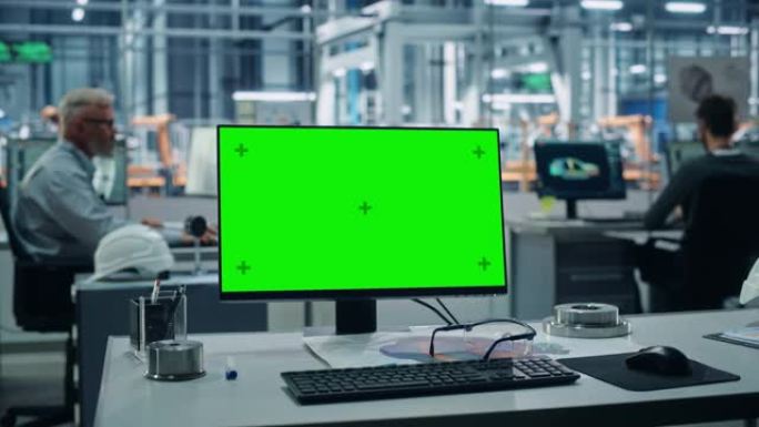 汽车厂: 桌上绿屏色度钥匙电脑。背景技术不同的工程师团队在自动化机械臂装配线制造车辆办公室工作