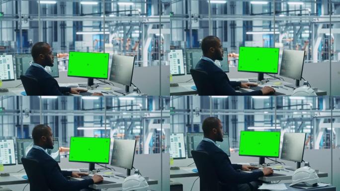 车厂办公室: 黑工程师在一台电脑上工作，两个监视器屏幕显示色键绿屏和监控自动化机械臂装配线制造高科技