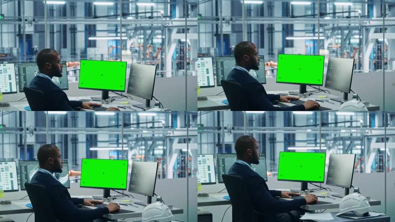 车厂办公室: 黑工程师在一台电脑上工作，两个监视器屏幕显示色键绿屏和监控自动化机械臂装配线制造高科技