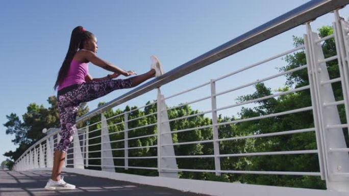 非裔美国妇女在城市大桥的栏杆上伸展腿
