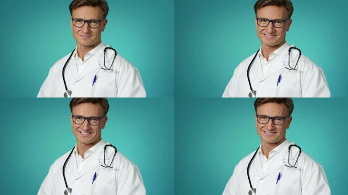 穿着白色实验室外套的英俊医生，听诊器对着镜头微笑，慢动作。诊所的医疗专业人员以积极的情绪看待。特写面