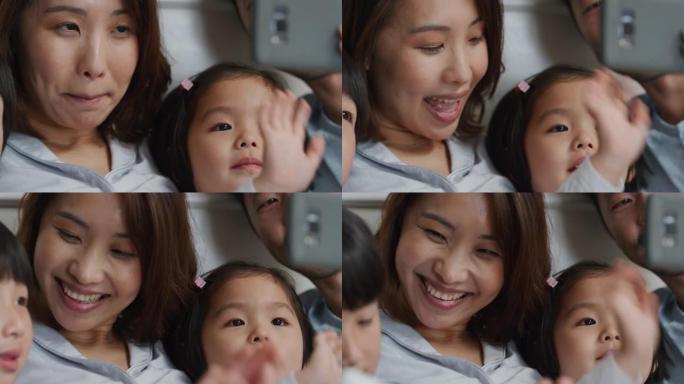 快乐的亚洲家庭在床上使用智能手机进行视频聊天母亲和父亲，孩子们在手机上挥舞着与朋友聊天，享受在线交流