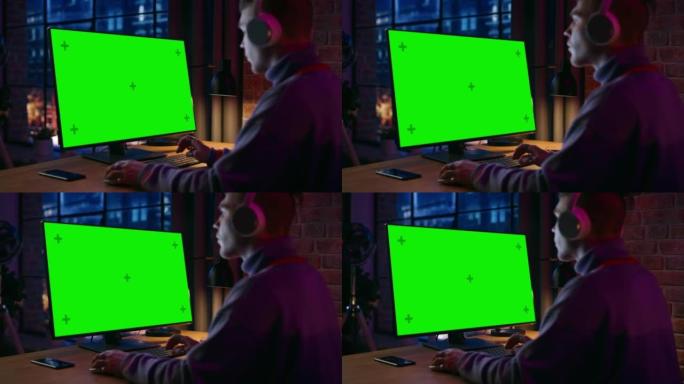 戴着耳机的年轻帅哥在家工作，台式电脑上有绿屏模拟显示。创意男性查看社交媒体，浏览互联网。从大窗户可以